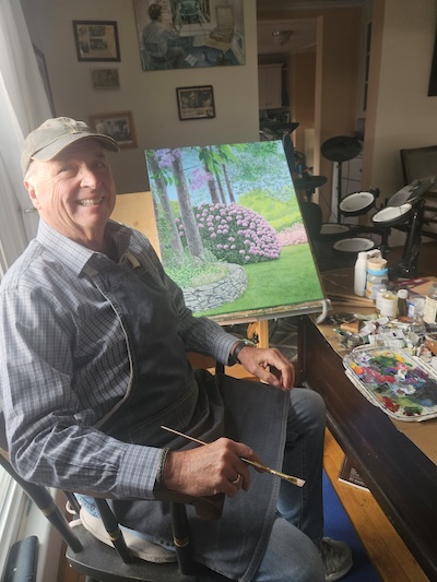 Portrait of artist Jim Belcher sitting in front of a painting in progress in his studio.