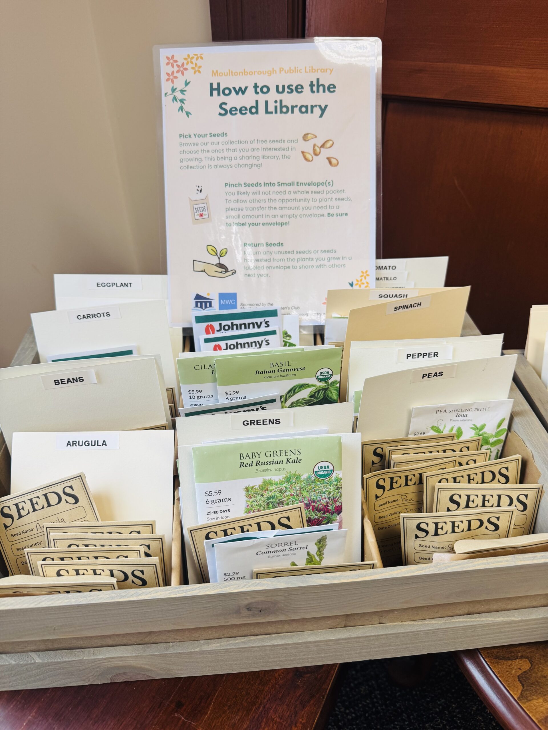 A tray of seed packets in our Seed Library with a poster outlining how to use it. 