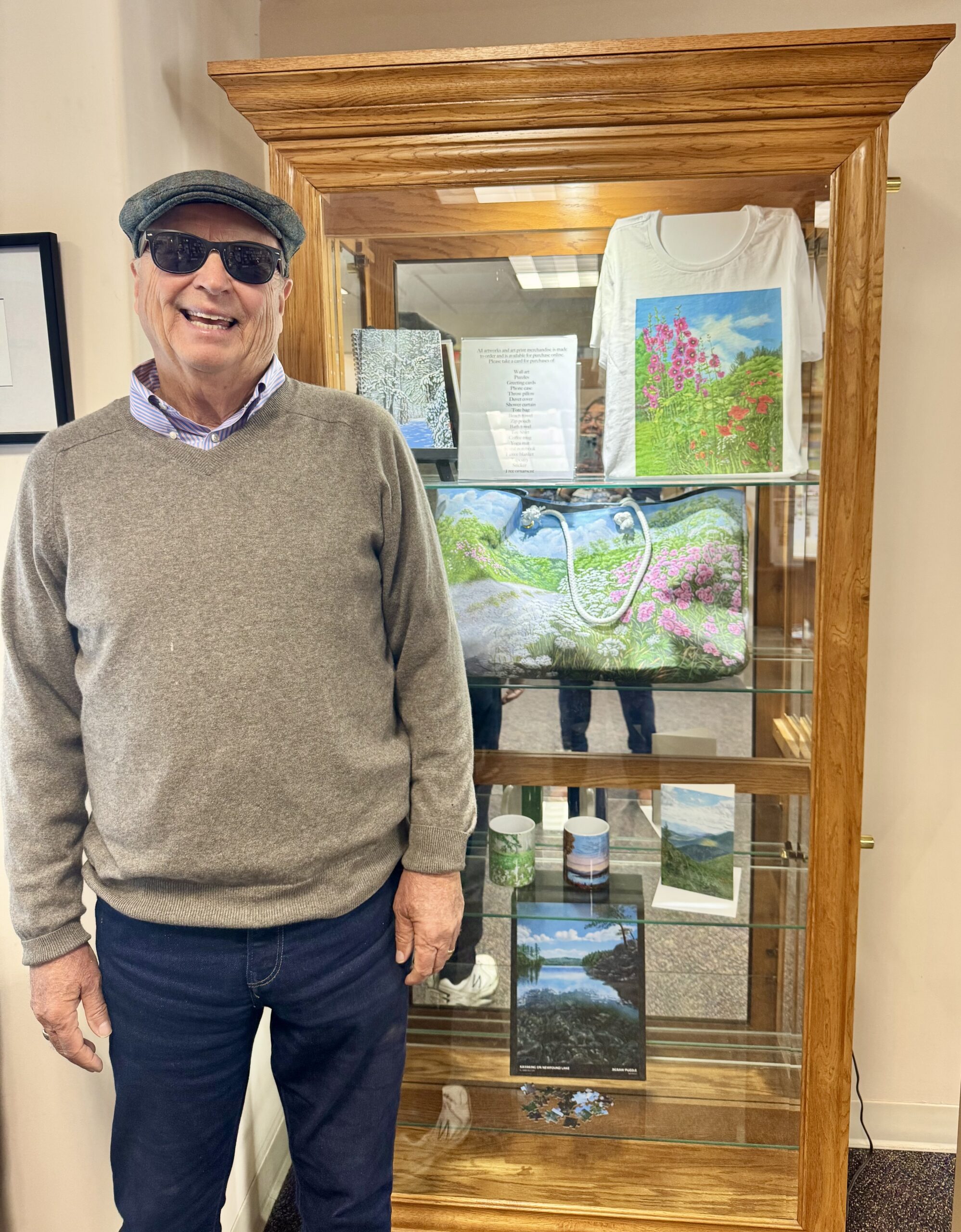 Artist Jim Belcher stands in front of the library's display case which holds an exhibit of some of the merchandise patrons can make from his artwork. 