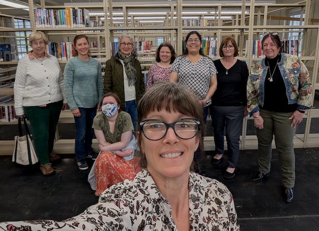 Moultonborough Library staff pose with Accesibility Services coordinator Deb Dutcher in front of shelves with large print books at the NH State Library Talking Books Collection.