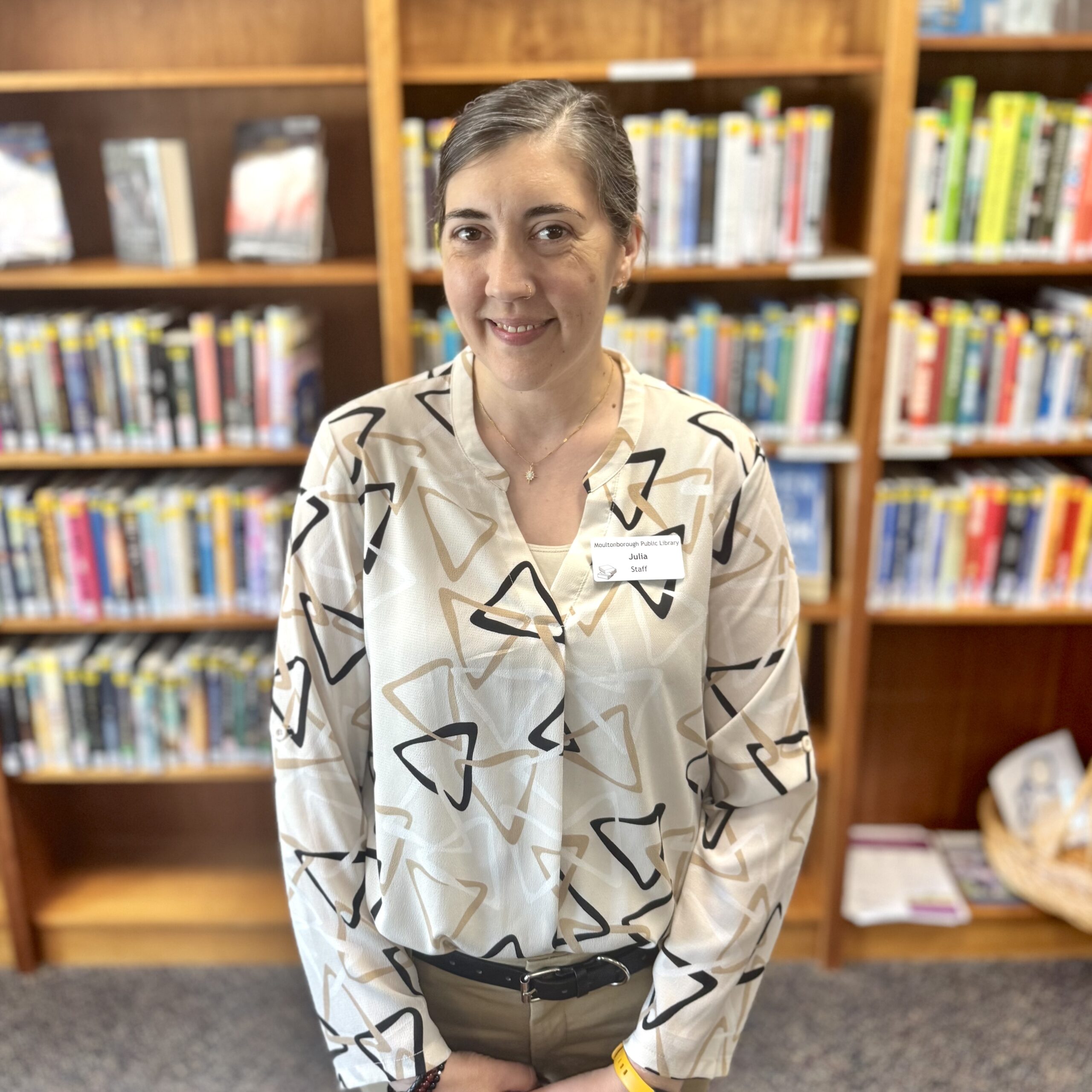Julia Chesley, new library assistant, poses in front of a shelf full of books