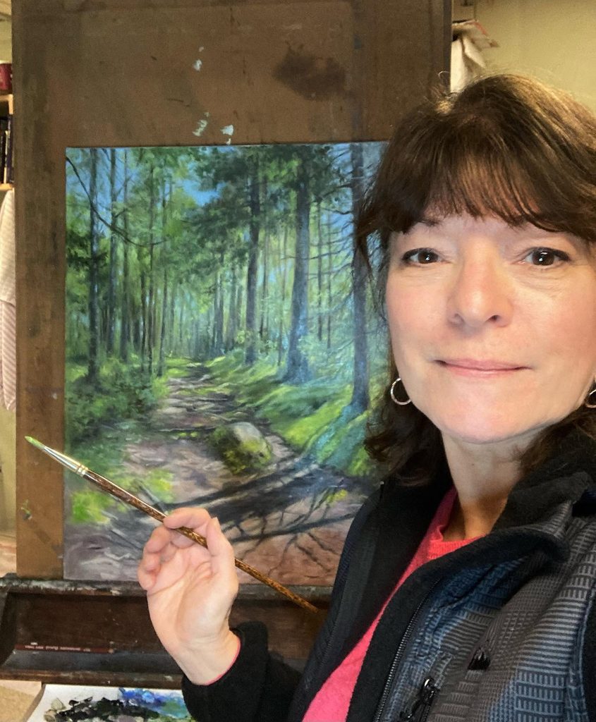 Jaylene Bengston stands in front of a piece of her art work with a oil paint brush in her hand.