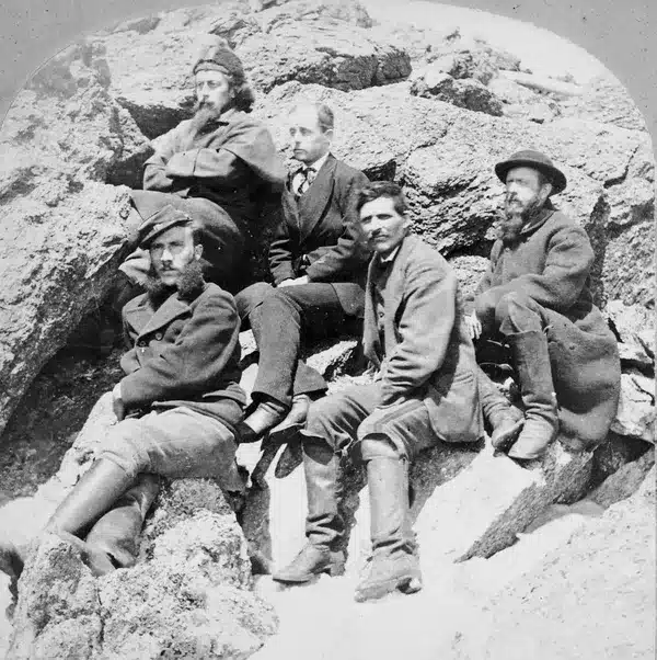 Black and white photo 5 men in 19th century winter gear pose on rocks on Mount Washington.