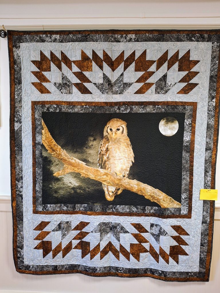 Quilted owl on a branch under a full moon. Chevrons in seasonal colors frame the owl.